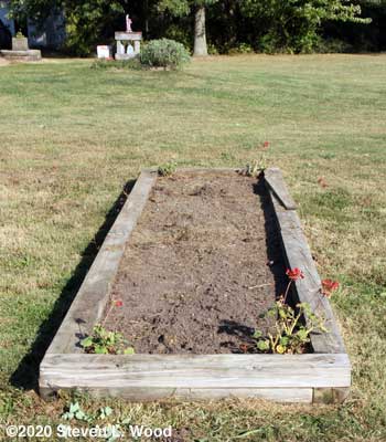 Narrow raised bed cleared of tomato plants, cages, and mulch